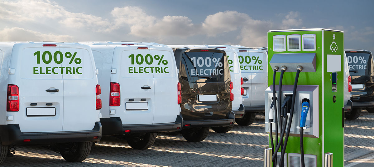 A collection of vans with the words "100% electric" on them, and an electric vehicle charging point.