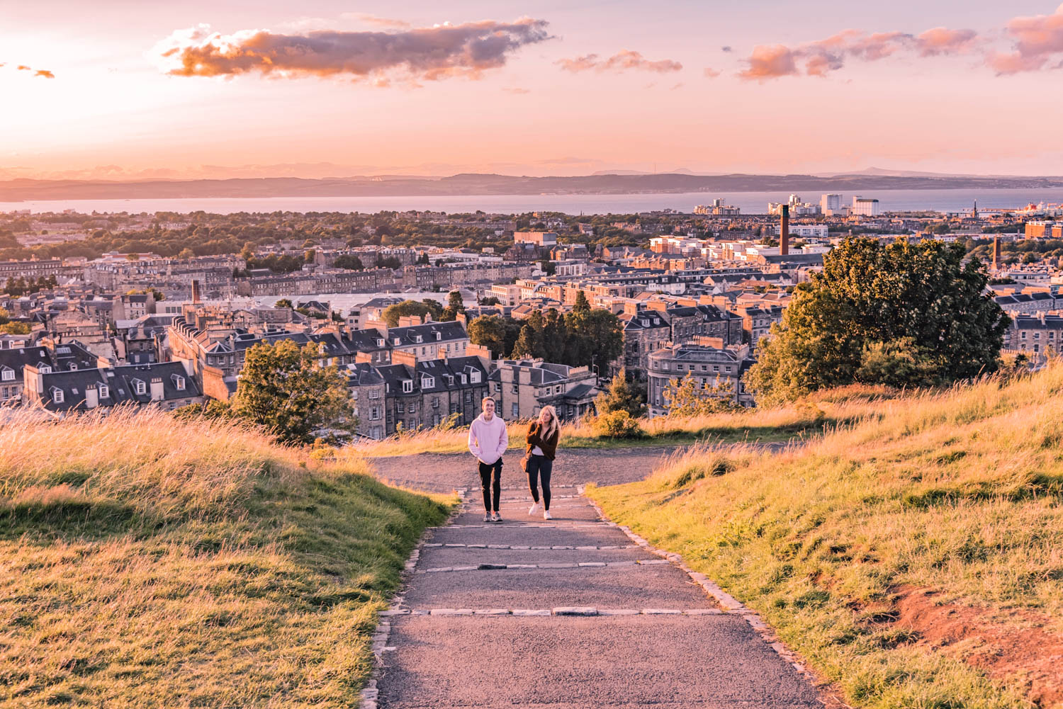 Two people walking up a hill with Edinburgh in the background