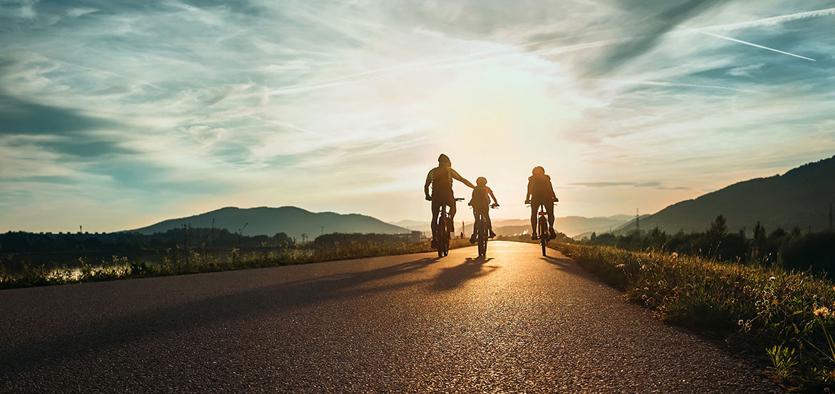 A family of three cycling along a road on a sunny day
