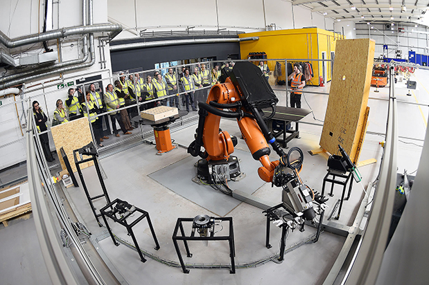 A group of people watch a robot arm perform a task in a factory.