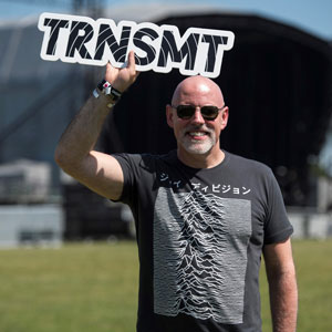 A man in a black and white tshirt, holding a sign saying TRNSMT