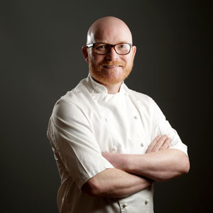 A man with glasses, wearing a chef's jacket.