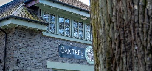 An exterior shot of a grey stone building, with green framed windows and a sign saying Oak Tree.