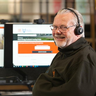 man in black shirt sitting in front of a desktop screen, wearing a headset