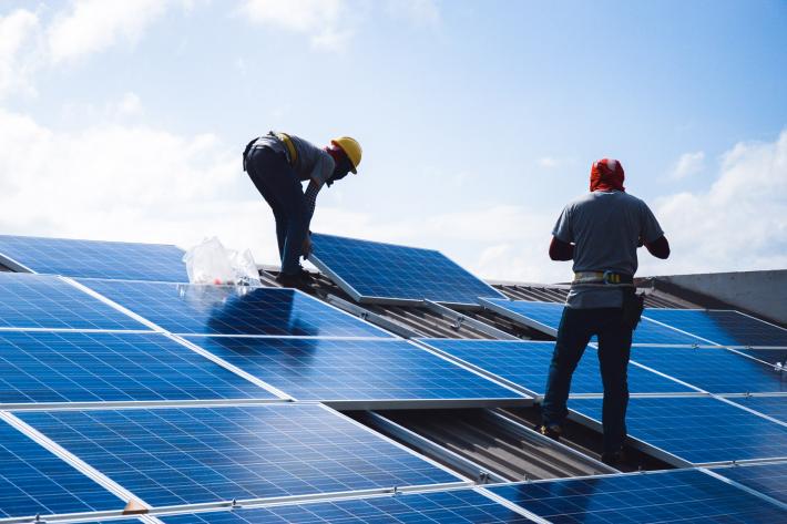 Two workers applying solar panels to the roof of a house