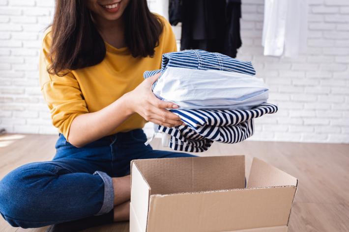 A woman putting in a pile of white and blue stripey tops into a cardboard box