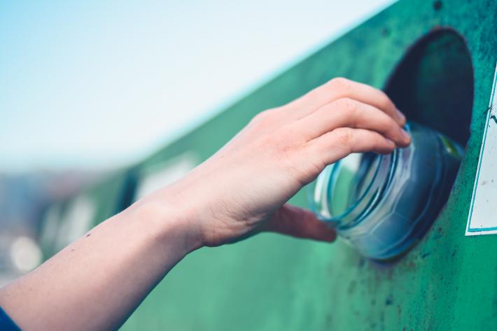 A hand putting a glass container into a recycling bin