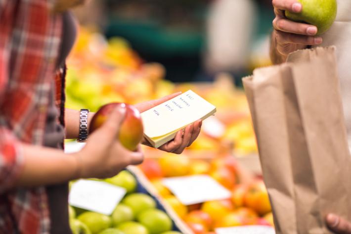 Two people in the shop holding apples and a shopping list