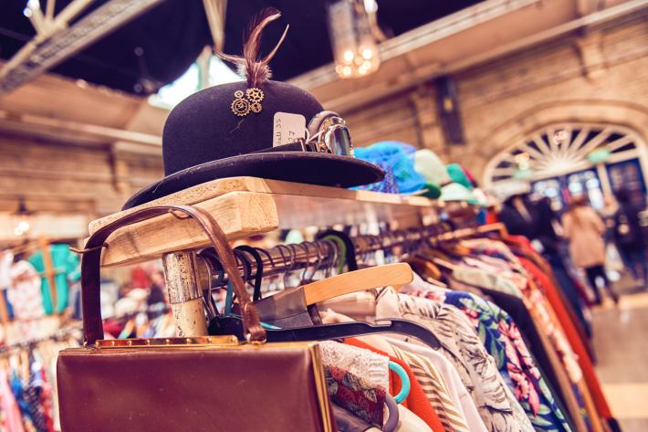 A bowler hat on top of a clothes rail with vintage clothes.