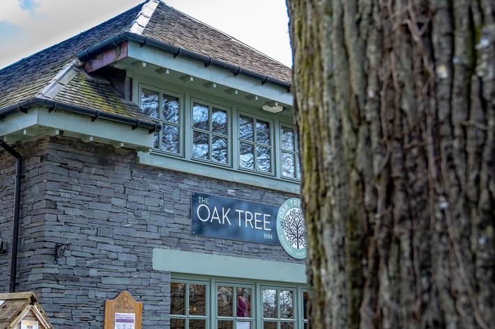 An exterior shot of a grey stone building, with green framed windows and a sign saying Oak Tree.