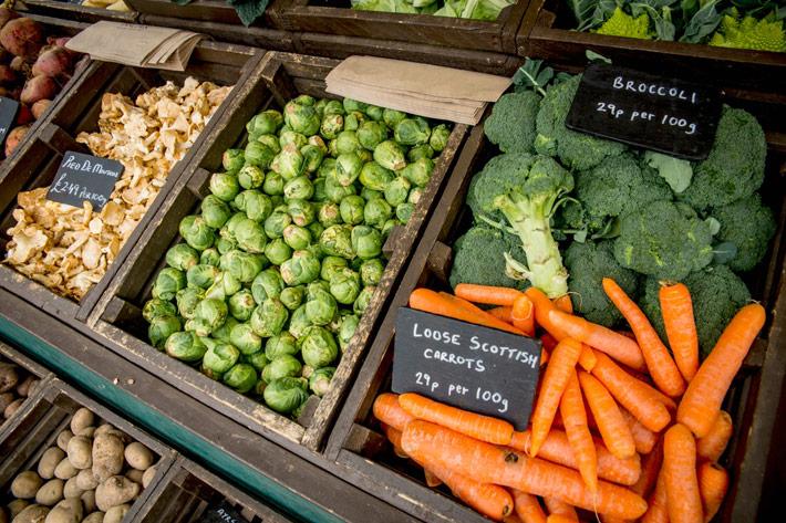 A selection of fresh vegetables, including carrots, broccoli and sprouts for sale in a greengrocers