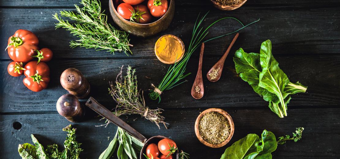 Vegetables, herbs and spices spread around a wooden board. Some of them are in the pots, spoons or bowls.