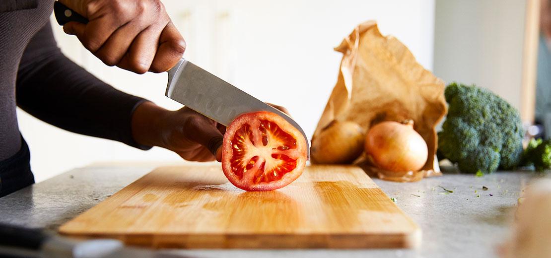 A person chopping a tomato on a wooden chopping board.