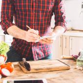 A man in a checked shirt writing on a shopping list