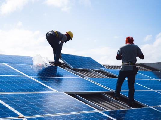 Two workers applying solar panels to the roof of a house