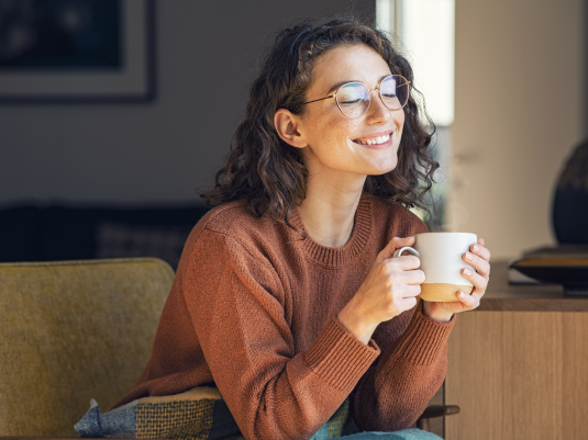 woman wearing glasses and brown shirt sitting on sofa and holding a white mug